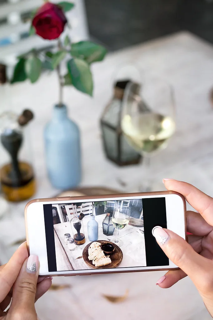 Manos sosteniendo un teléfono para fotografiar un plato en una mesa